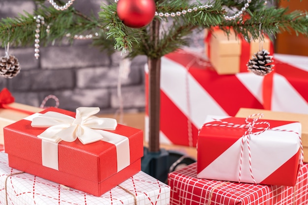 Árbol de Navidad decorado con hermosos regalos envueltos en rojo y blanco en casa con pared de ladrillo negro, concepto de diseño festivo, de cerca.