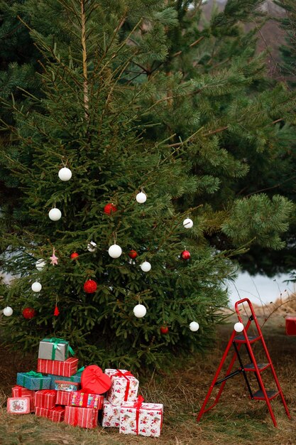 Árbol de Navidad decorado con juguetes en la naturaleza Colores rojo y blanco Muchos regalos envueltos cerca del árbol de Navidad Escaleras rojas