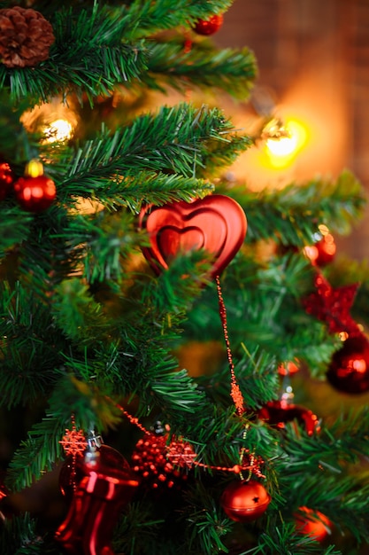 Árbol de Navidad decorado con juguetes rojos, adornos, conos de pino, luces bokeh de perlas de primer plano oscuro