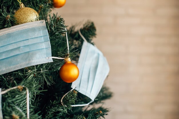 Árbol de Navidad decorado con máscaras médicas azules y bolas doradas, de cerca. Concepto del año nuevo 2021 en medio de la pandemia de coronavirus. Símbolo de fiesta en cuarentena. Imagen con espacio para texto.