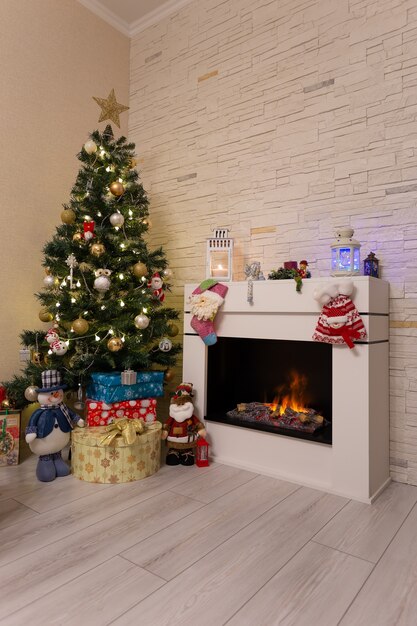 Árbol de Navidad decorado, regalos y adornos navideños cerca de la chimenea encendida