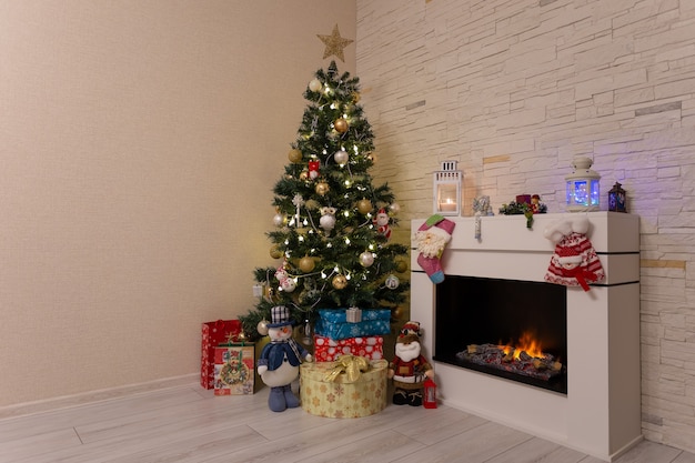 Árbol de Navidad decorado, regalos y adornos navideños cerca de la chimenea encendida