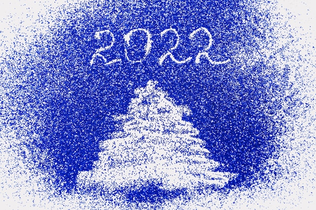 Árbol de navidad dibujado con el dedo y número 2022 sobre fondo de confeti azul brillante