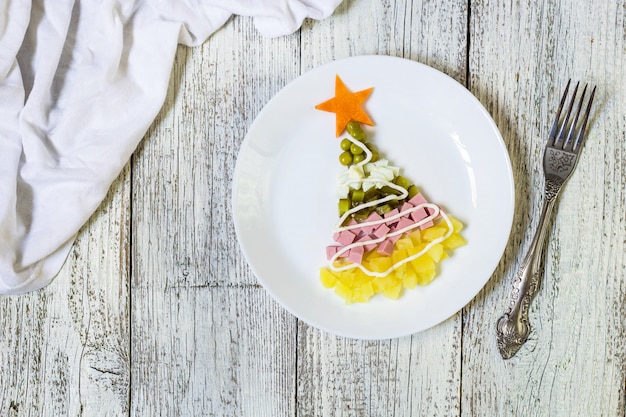 Árbol de Navidad de una ensalada más olivier en placa sobre una mesa de madera blanca. Vista superior con un espacio de copia