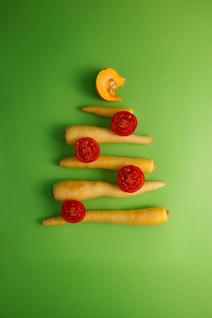 Árbol de Navidad ensamblado a partir de verduras, tomates, zanahorias, champiñones en una vista superior de fondo verde