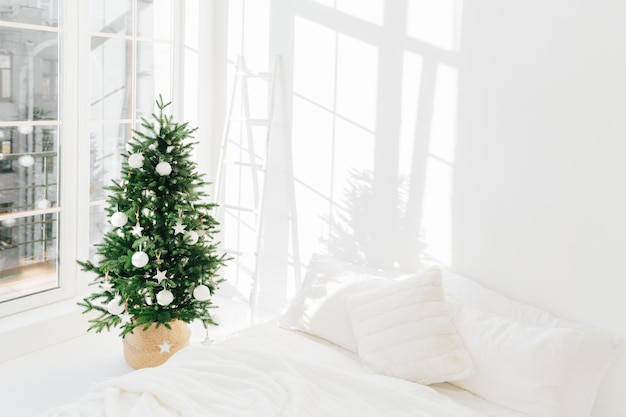 Árbol de Navidad festivo decorado en interior de dormitorio clásico blanco con cama suave Interior de casa de invierno Temporada acogedora Celebración de Año Nuevo