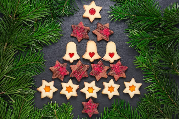 Árbol de Navidad de galletas linzer caseras con mermelada de frambuesa y estrellas de chocolate con crujidos de frambuesa en mesa de pizarra con ramas de pino