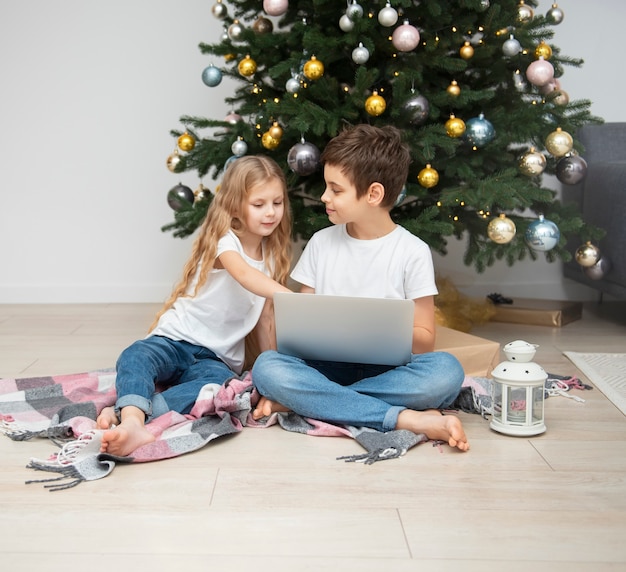 Árbol de Navidad en una gran sala de estar. Los niños juegan cerca del árbol de Navidad. Un niño con una computadora portátil se comunica con sus amigos.