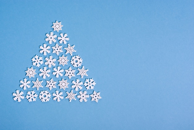 Árbol de Navidad hecho de copos de nieve blancas sobre fondo azul.