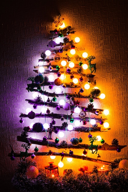 Árbol de navidad hecho de ramitas y palos con luces púrpuras y naranjas en la noche.