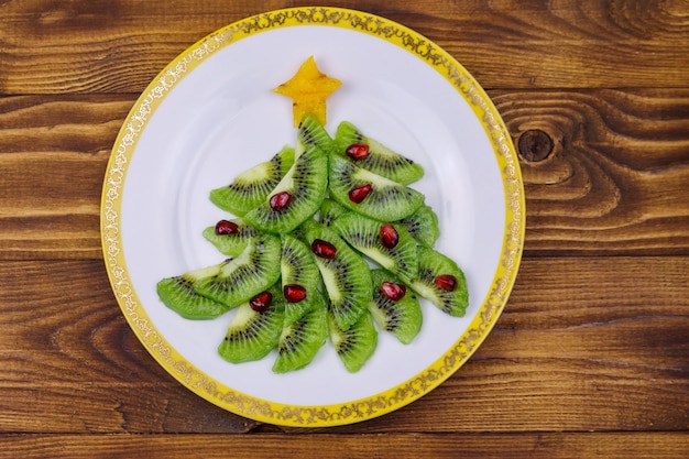 Árbol de Navidad hecho de rodajas de kiwi y granada en mesa de madera. Vista superior. Idea creativa para postres festivos de Navidad y año nuevo. Idea divertida de comida para niños