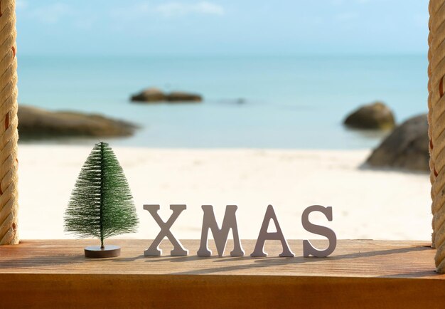 Árbol de Navidad y inscripción XMAS en una playa de arena con flores