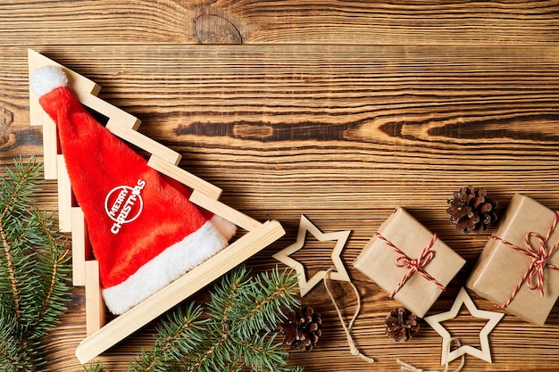 Árbol de navidad de madera con gorro de Papá Noel dentro de cajas de regalo ramas de abeto conos de pino y estrellas de madera