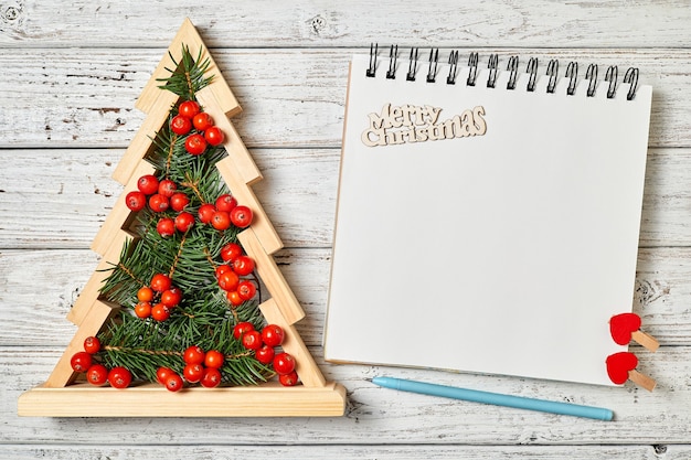 Árbol de Navidad de madera con ramas de abeto y bayas de serbal dentro del Bloc de notas en blanco sobre fondo de madera