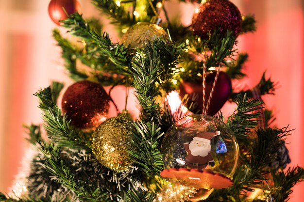 Árbol de Navidad montado con adornos. Bolas rojas, plateadas y doradas, cajas regalo, luces, Papá Noel y otros. Enfoque selectivo.