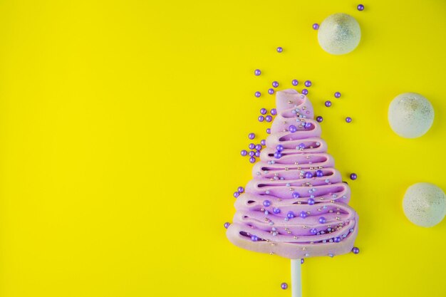 Árbol de navidad morado pálido hecho de merengue en un palo decorado con bolas moradas y plateadas sobre un b ...