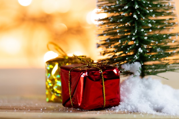 Árbol de navidad en la nieve blanca con el regalo y los fondos ligeros del bokeh