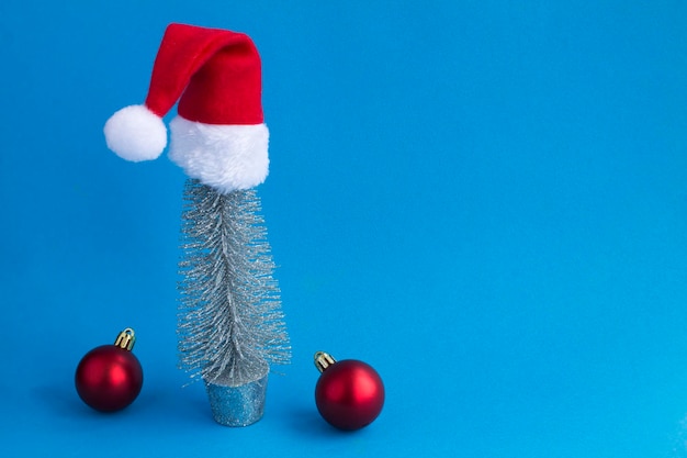 Árbol de Navidad plateado con sombrero de Papá Noel en el fondo azulCopiar espacio Primer plano