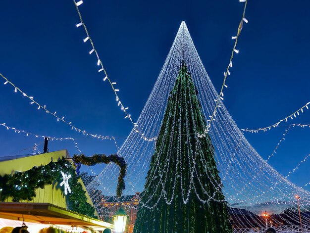 Árbol de Navidad resplandeciente con adornos y mostradores de Navidad instalados en la Plaza de la Catedral de Vilnius, Lituania. Tiene luces de hadas como si fuera un velo de novia. Iluminado por la noche