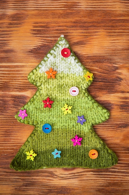 Árbol de Navidad tejido con botones sobre fondo de madera. Concepto de vacaciones de Navidad