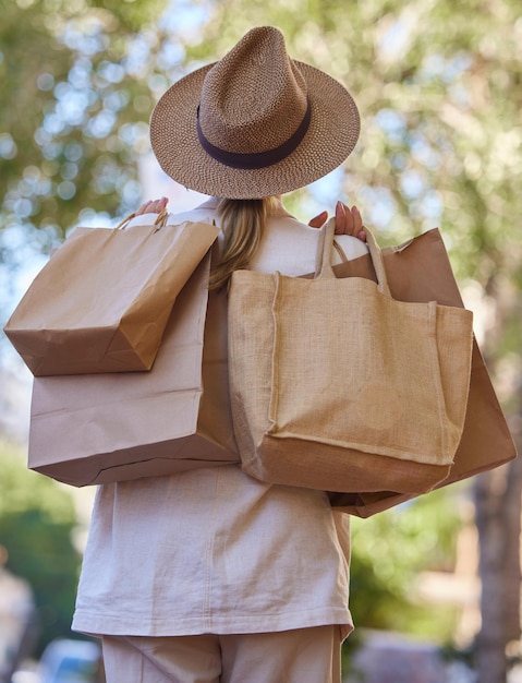 Árboles de sol y mujer con bolsas de compras desde atrás caminando en el parque de vacaciones Naturaleza de verano y chica de viaje con bolsa de compras de boutique de diseñador de lujo comprando regalos en el camino del jardín de vacaciones