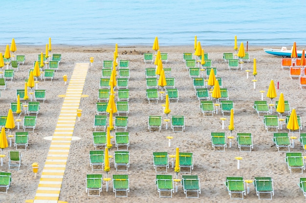 Área de lounge na praia com guarda-sóis amarelos e espreguiçadeiras verdes na costa italiana.