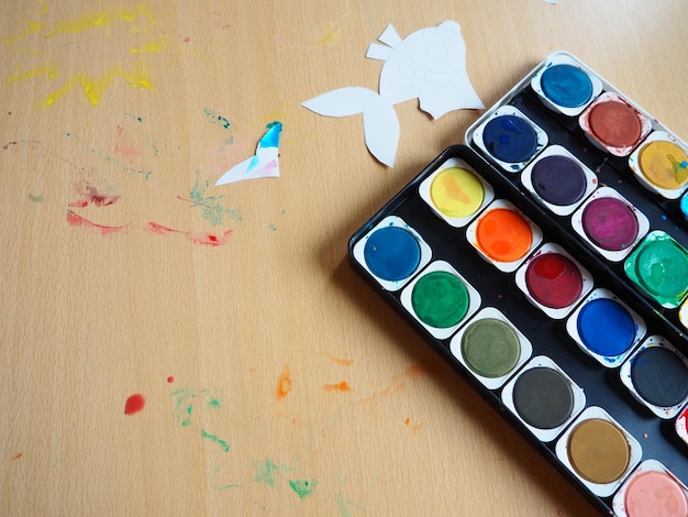 Área de trabalho com ferramentas de desenho Um conjunto de tintas em aquarela Estatuetas de peixes pintadas com recorte de papel Vista de cima Lição ou tarefa criativa