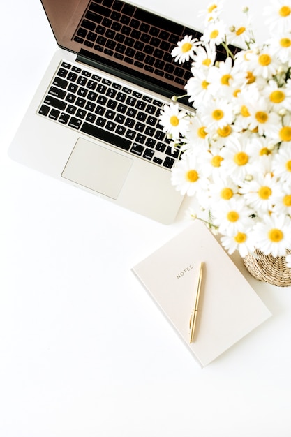 Área de trabalho da mesa do escritório doméstico com laptop, buquê de camomila e caderno na superfície branca