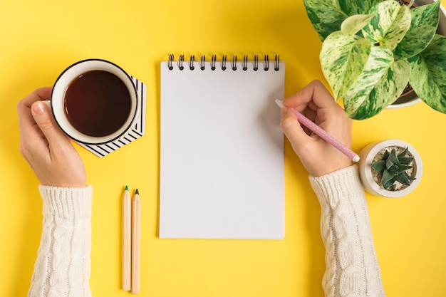 Área de trabalho das mãos de uma mulher escrevendo no bloco de notas em branco