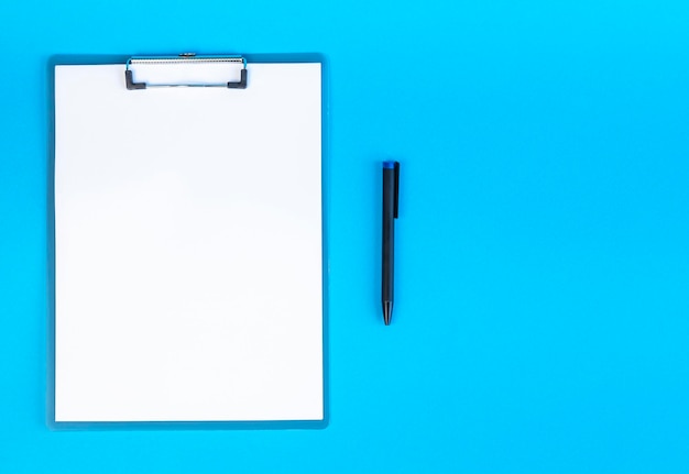 Área de transferência com folha em branco de papel branco e caneta no lugar de fundo azul para texto