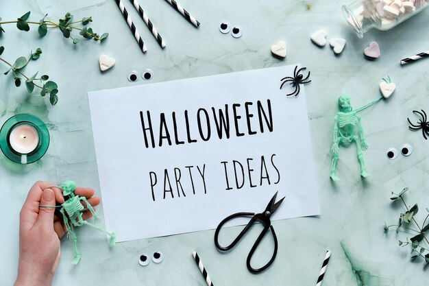 Área de transferência com ideias de festa de Halloween de texto em fundo verde menta. Plano plano com o esqueleto na mão,