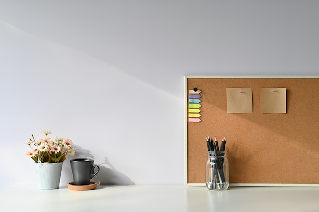 Área de trabajo café, lápiz, flor y una nota adhesiva a bordo con escritorio de oficina y luz de la mañana.