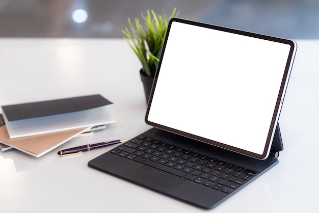 Área de trabajo tableta pantalla en blanco con bloc de notas una mesa colocada en la oficina.