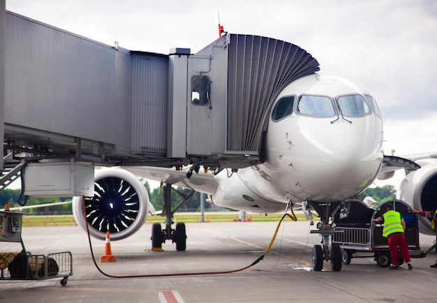 Foto reabastecimiento de combustible del avión en el aeropuerto antes de la salida el avión blanco está en la plataforma los pasajeros se sientan a través del puente de embarque servicio de manejo