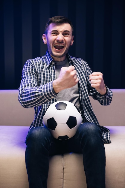 Foto la reacción gratamente sorprendida de un joven está viendo la televisión y sentado en el sofá reacción de los fanáticos de los deportes