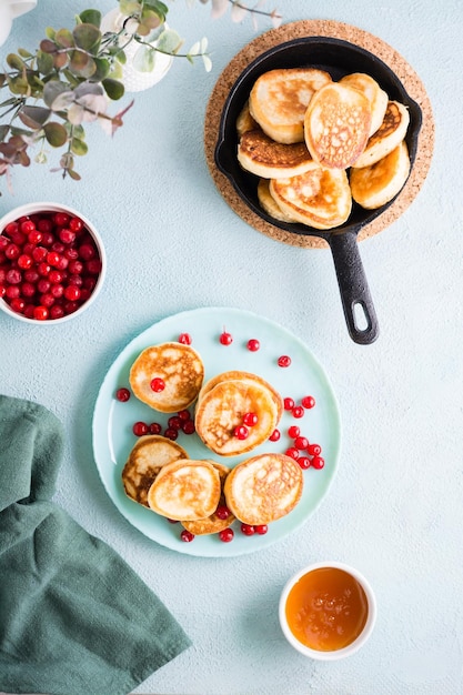 Foto readytoeat pfannkuchen und preiselbeeren auf einem teller und pfanne mit pfannkuchen auf dem tisch hausgemachtes frühstücksdessert ansicht von oben und vertikal