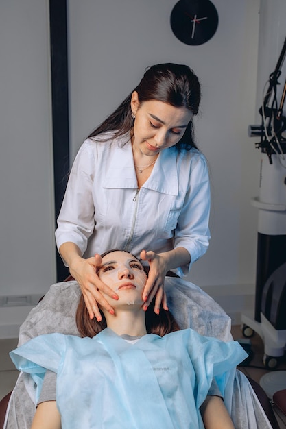 Realização de um procedimento de cuidados com a pele em um salão de spa. Um cosmetologista presta um serviço de beleza aplicando uma máscara de tecido com vitaminas no rosto da garota.