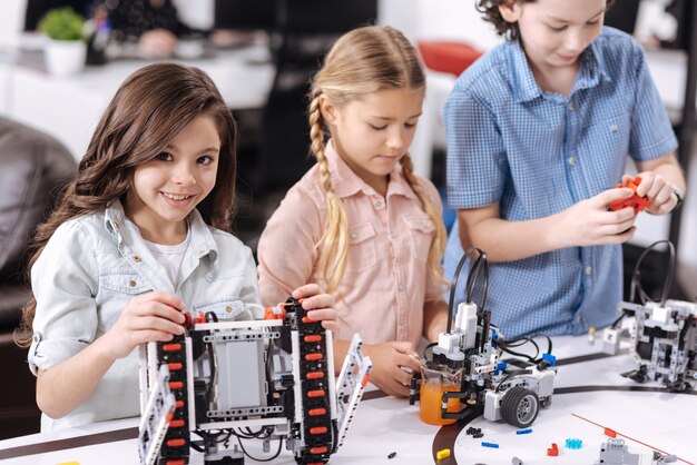 Realizando nuestro proyecto científico. Carismáticos encantados escolares encantadores sentados en la escuela y probando dispositivos cibernéticos mientras tienen una lección de ciencias