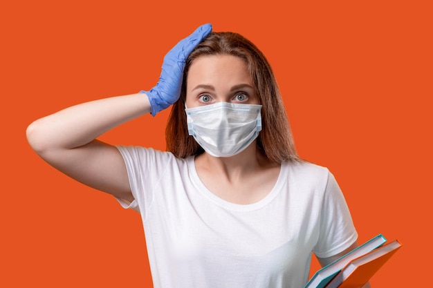 Reapertura de la escuela Ansiedad de cuarentena Estudiante perturbada con guantes de mascarilla protectora tocando la cabeza aislada en el espacio de copia rojo naranja COVID19 pandemia Educación segura