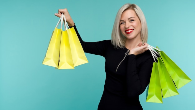 Rebaja. Mujer sonriente joven con bolsas de la compra en la fiesta del viernes negro. Niña feliz sobre fondo azul