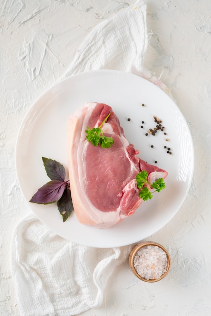 Rebanada de cerdo grasa cruda o bistec en un plato de cerámica blanca con especias y hierbas aisladas