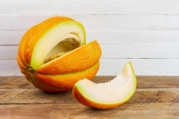 Una rebanada cortada de melón amarillo dulce maduro sobre una mesa de madera sobre un fondo blanco de madera con un espacio de copia