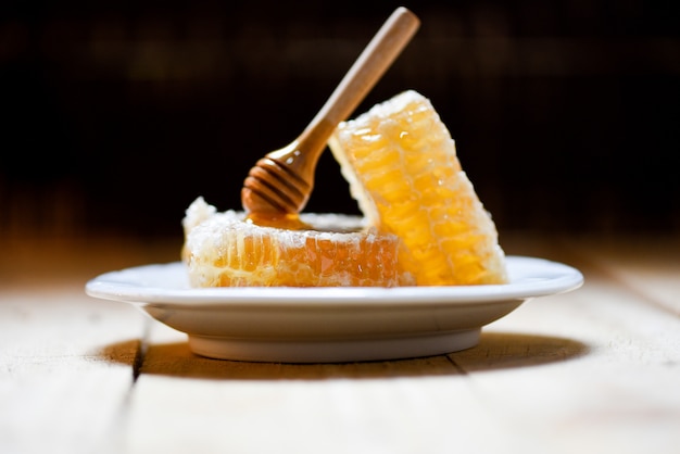 Rebanada dulce del panal del amarillo de la comida sana fresca de la miel con el cazo de madera en la placa y la oscuridad