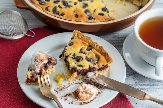 Rebanada fresca de tarta de cerezas con helado y taza blanca con té sobre un fondo de madera, cerrar