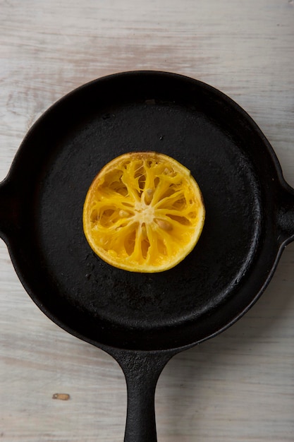 Rebanada de fruta cruda de naranja en una sartén de hierro sobre un piso de madera