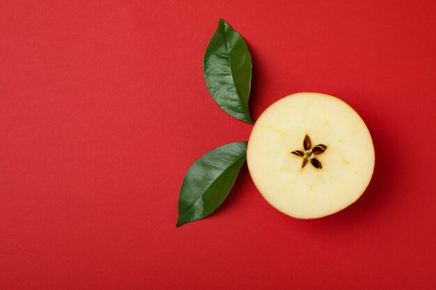 Rebanada de manzana con hojas sobre fondo rojo.