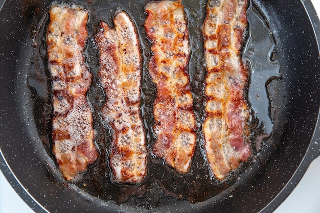 Rebanada o tira de tocino frito crujiente y ahumado Ingrediente de engorde de alimentos grasos no saludables Rojo Rebanada o tira delgada o lonchas de tocino se fríen en una sartén grasa de cerdo derretida Comida alta en calorías Idea de desayuno