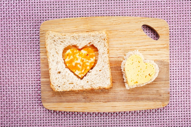 Rebanada de pan con corte en forma de corazón y queso sobre fondo de madera