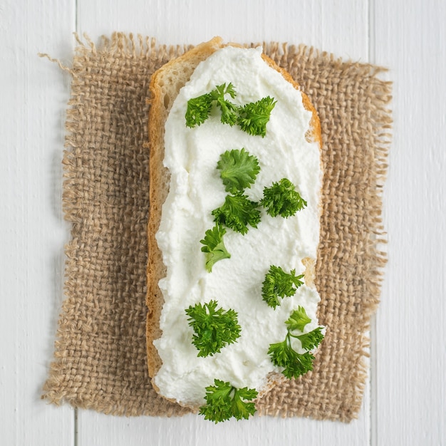 Una rebanada de pan fresco con crema de queso cottage con vista superior de perejil.