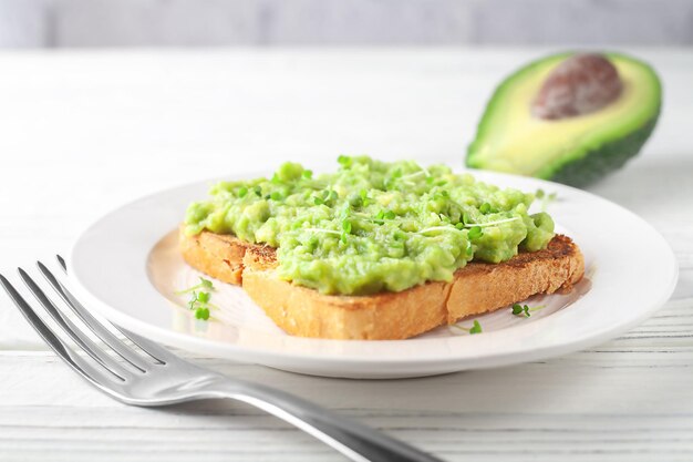 Una rebanada de pan fresco en un plato con aguacate sobre un fondo de tablas de madera ligera